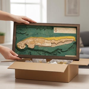 Könnte beinhalten: Ein rechteckiges Wandbild mit Holzrahmen, das eine mehrschichtige bathymetrische Karte von Norderney zeigt. Die Karte stellt tiefgrüne Wassertiefen, eine beigefarbene Landmasse und einen gelben Sandstrand dar, eingefasst in einen dunkelbraunen Holzrahmen.