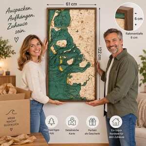 May include: A rectangular wooden bathymetric map of the North Sea coast featuring deep teal water layers and tan land masses. The map measures 122 cm by 61 cm with a 6 cm frame depth. Text on the map includes Auspacken, Aufhangen, Zuhause sein.