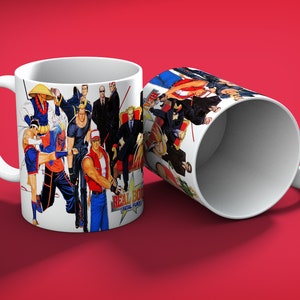 May include: Two white ceramic mugs with a colorful graphic design featuring characters from the video game "Real Bout Fatal Fury." The mugs are on a red background. One mug is upright, and the other is tilted.