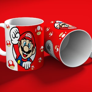 May include: Two white ceramic mugs with a red background. One mug features a cartoon image of Mario, the other has a controller graphic. Both mugs have a red and white design with mushroom graphics.