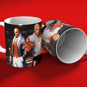 May include: White ceramic mug featuring a vibrant illustration of two male characters from a fighting game. One mug is upright, the other is tilted, showcasing the full wrap-around design against a red background. The characters are depicted in action poses.