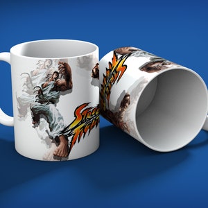 May include: Two white ceramic mugs with a Street Fighter graphic. One mug is upright, the other is tilted. The graphic features a muscular character in a white gi, with the words "Street Fighter" in yellow and orange.
