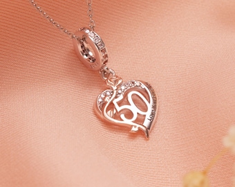 Puede incluir: Un collar plateado con un colgante en forma de corazón. El colgante presenta el número "50" y está adornado con pequeñas piedras preciosas transparentes. El collar tiene una cadena delicada y un dije circular con más piedras preciosas. Las palabras "Love You Forever" están inscritas.