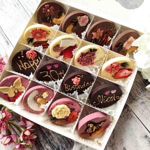 May include: A white box filled with 16 round chocolate discs. The chocolates are decorated with various designs, including flowers, butterflies, hearts, and text. The text on the chocolates includes "Happy 30th Birthday" and "Nicola".