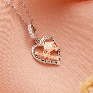 Peut inclure: Collier avec pendentif en forme de cœur en argent avec un bonnet de diplômé et un diplôme à l'intérieur. Le pendentif porte l'inscription "She believed she could so she did".