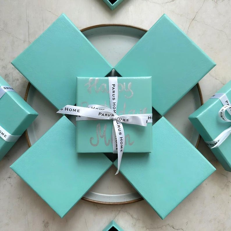 Puede incluir: Varias cajas de regalo turquesas, algunas con cintas blancas. La caja central est&aacute; envuelta con una cinta con la inscripci&oacute;n "PARUS HOME" y "Happy Mother's Day" en plata. Las cajas est&aacute;n dispuestas sobre una superficie neutra.