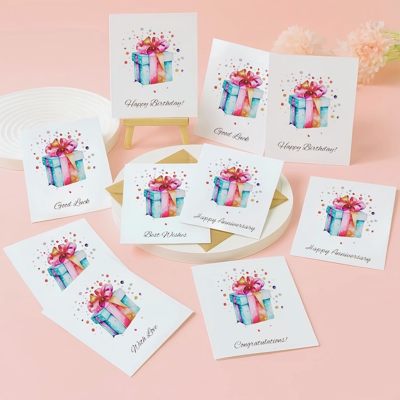 Puede incluir: Un conjunto de tarjetas de felicitaci&oacute;n blancas con ilustraciones de acuarela de cajas de regalo con lazos rosas. Las tarjetas tienen varios mensajes, incluyendo "Happy Birthday!", "Good Luck", "Best Wishes", "Happy Anniversary", "With Love" y "Congratulations!"