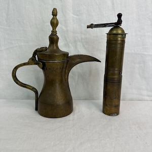 May include: A brass coffee pot with a long spout and a handle, and a brass coffee grinder with a wooden handle.
