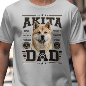 May include: A light gray t-shirt featuring an Akita dog with the word "AKITA" above the dog's image. Below the dog is the word "DAD" with a paw print. The shirt also includes the words "Loyal, Dignified, Fearless, Protective, Courageous, Devoted".