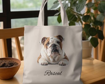 May include: A beige tote bag featuring a detailed illustration of a bulldog with brown and white markings. The word "Rascal" is written in cursive below the dog. The bag has cream-colored handles.