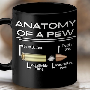 May include: Black coffee mug with white text that reads "Anatomy of a Pew". The mug features a diagram of a bullet with labels for "Bang Button", "Freedom Seed", "Metal Holdy Thing", and "Magical Fire Dust".