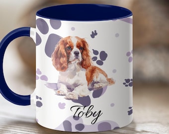 May include: White ceramic mug with a navy blue interior and handle. The mug features a watercolor illustration of a Cavalier King Charles Spaniel dog, the name "Toby" in script, and paw print designs.