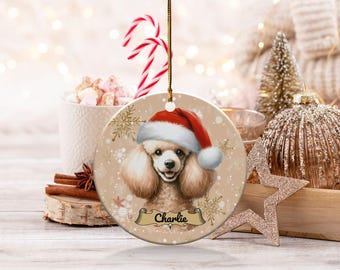 May include: A round ceramic Christmas ornament featuring a white poodle wearing a red Santa hat. The ornament has a gold glitter background with snowflakes and the name "Charlie" written on a banner.