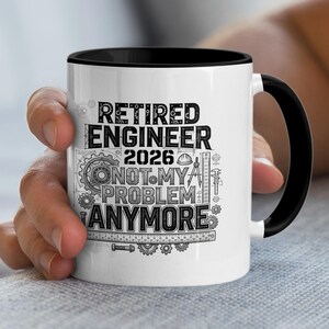 May include: A white ceramic mug with a black interior and handle. The mug features the text "RETIRED ENGINEER 2026 NOT MY PROBLEM ANYMORE" in black, along with engineering-related graphics. The mug is held by a person.