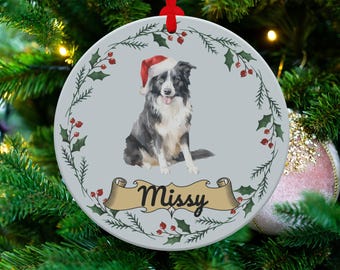 Könnte beinhalten: Runder Weihnachtsschmuck mit einem Border Collie im Aquarellstil, der einen Weihnachtsmannhut trägt. Der Schmuck hat einen hellblauen Hintergrund mit einem Stechpalmen- und Beerenrand. Der Name des Hundes, "Missy", wird auf einem Banner angezeigt.