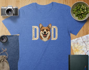 May include: A blue t-shirt with a white graphic of a corgi dog with the word "DAD" on either side of the dog.