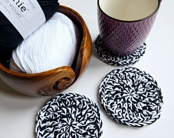 Pode incluir: Quatro  costuras de crochê preto e branco com uma caneca em cima de uma delas. A caneca é roxa com uma superfície texturizada. Há duas bolas de fio no fundo, uma branca e outra preta.