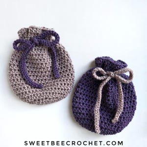 May include: Two crocheted drawstring bags, one in a light brown and purple colour combination and the other in a dark purple and light brown colour combination. The bags are made with a textured stitch and have a simple bow tie closure.