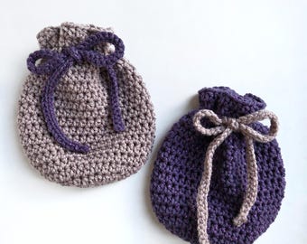 May include: Two crocheted drawstring bags, one in a light brown and purple colour combination and the other in a dark purple and light brown colour combination. The bags are made with a textured stitch and have a simple bow tie closure.