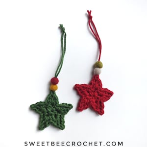 May include: Two crocheted star ornaments. One is green with red and yellow beads, the other is red with green and white beads. Both have a loop for hanging. The text "SWEETBEE CROCHET.COM" is at the bottom.
