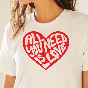 May include: White t-shirt with a red heart graphic that says "All you need is love" in white lettering.