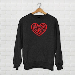 May include: A dark gray sweatshirt with a red heart graphic that says "All You Need Is Love" in a stylized font.