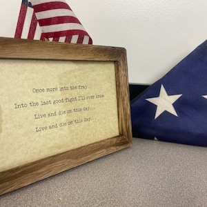 以下が含まれることがあります： この日に戦うことと死ぬことについて書かれた詩が額装されたプリント。詩の内容は「Once more into the fray... Into the last good fight I'll ever know. Live and die on this day.... Live and die on this day...」。額縁の右側に折り畳まれたアメリカ国旗がある。