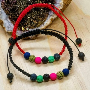 Puede incluir: Dos pulseras con cordones negros y rojos y cuentas de roca volcánica. Una pulsera tiene cuentas verdes, rosas y azules. La otra pulsera tiene cuentas azules, verdes y rosas.