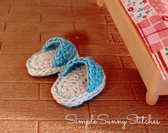 Op de afbeelding: Een paar blauwe en witte gehaakte sloffen. De sloffen zijn klein en staan op een houten vloer. De tekst "Simple Sunny Stitches" is zichtbaar in de rechterbenedenhoek van de afbeelding.