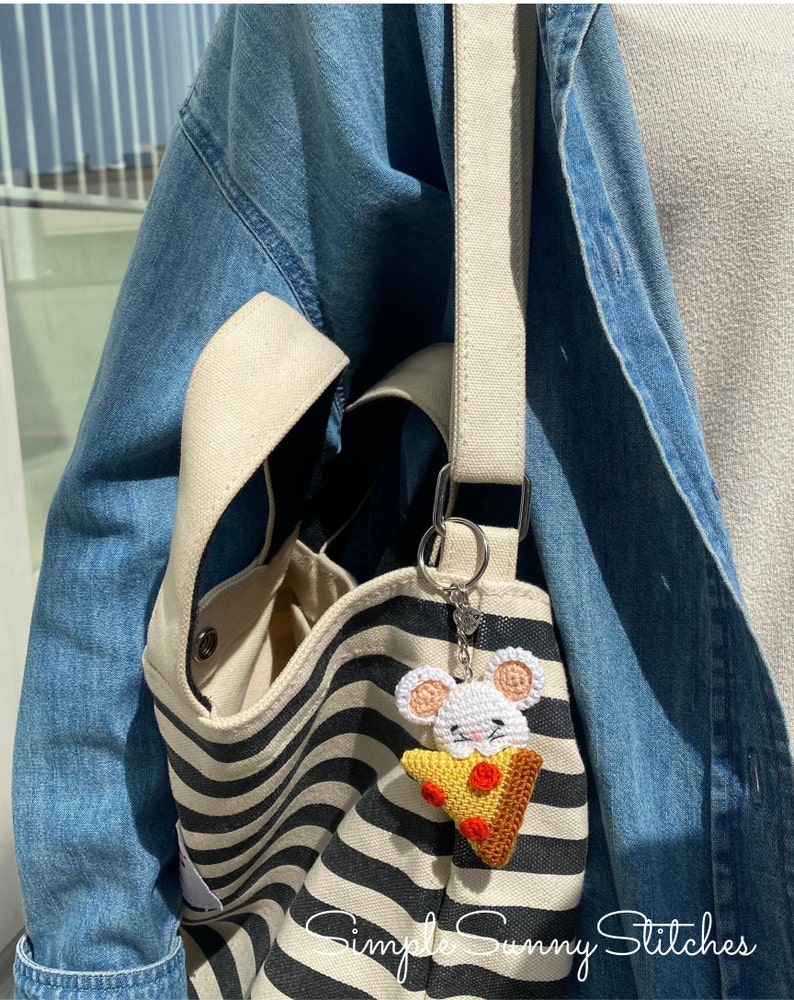 May include: A white crocheted mouse holding a slice of pizza with red pepperoni, attached to a black and white striped tote bag with a beige strap. The bag has a small pocket on the side. The text "Simple Sunny Stitches" is visible at the bottom of the image.