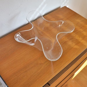 Op de afbeelding: Een doorzichtige plastic kom met een uniek, golvend, stervormig ontwerp staat op een houten oppervlak.