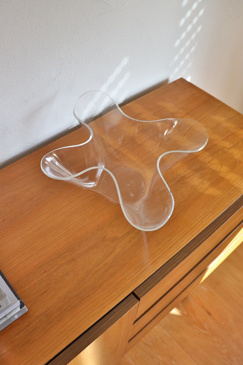 Op de afbeelding: Een doorzichtige plastic kom met een uniek, golvend, stervormig ontwerp staat op een houten oppervlak.