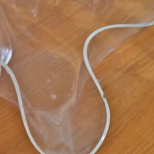 Op de afbeelding: Een doorzichtige plastic kom met een unieke, golvende, organische vorm. De kom staat op een houten oppervlak.