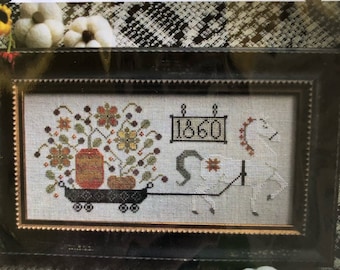 May include: A framed cross-stitch design featuring a white horse pulling a cart filled with pumpkins and autumn foliage. The cart is labelled "1860".