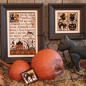 May include: Two framed cross-stitch patterns with a Halloween theme. One pattern features a black cat, an owl, a witch, and a jack-o-lantern. The other pattern features a poem about a pumpkin and a house with a black cat and an owl. The frames are brown wood and the patterns are on white fabric.