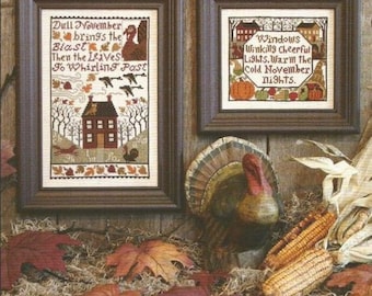 May include: Two framed cross-stitch patterns with autumn themes. The first pattern features a house with a red roof and the text "Dull November brings the Blast Then the Leaves To Whirling Past". The second pattern features a house with a red roof and the text "Windows Winkingly Cheerful Lights. Warm the Cold November nights."