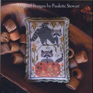 May include: A cross-stitch sampler featuring a design of three raccoons with a pumpkin. The sampler is titled "Raccoon Rabble" and is from Plum Street Samplers. The design is by Paulette Stewart.