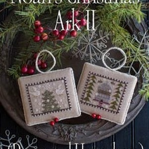 May include: Two cross-stitch ornaments with a Christmas theme. The first ornament features a Christmas tree with doves on either side. The second ornament features a small house with a snowy roof and pine trees. The text "Noah's Christmas Ark II (Doves and Honeybees)" is at the bottom of the image.
