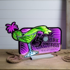 May include: A neon sign featuring a margarita glass with a palm tree and lime slice. The sign has the text "5 O'Clock Somewhere" and "Margaritaville" with a purple and white background. The sign is on a white base.