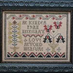 May include: A cross-stitch sampler with a beige background and colorful embroidery. The sampler features a floral design with red, blue, and yellow flowers. The text reads "Be kinder than necessary & love beyond measure."