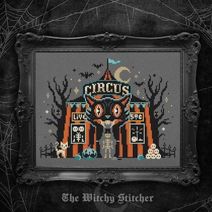 May include: A cross-stitch embroidery in a black ornate frame featuring a circus tent with orange and black stripes. The design includes a large black cat head, a skeleton, a small white cat, skulls, bats, and the text CIRCUS, LIVE, and 5¢.