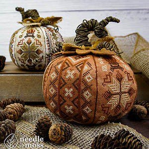 May include: Two fabric pumpkins featuring intricate cross-stitch embroidery in shades of brown, orange, and cream. Each pumpkin is topped with a twisted vine stem and fabric leaves. The embroidery displays geometric patterns and snowflake motifs.