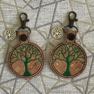 May include: Two cork and leather keychains with a green tree of life design. Each keychain has a silver charm with a tree of life design.