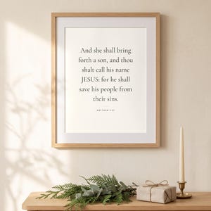 Peut inclure: Une impression d'art murale encadr&eacute;e avec le texte noir : And she shall bring forth a son, and thou shalt call his name JESUS: for he shall save his people from their sins. MATTHEW 1:21. L'impression est plac&eacute;e dans un cadre en bois clair.