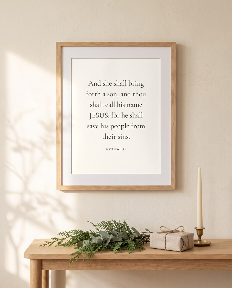 Peut inclure: Une impression d'art murale encadr&eacute;e avec le texte noir : And she shall bring forth a son, and thou shalt call his name JESUS: for he shall save his people from their sins. MATTHEW 1:21. L'impression est plac&eacute;e dans un cadre en bois clair.