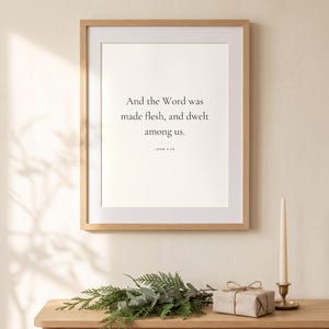 Peut inclure: Une affiche murale rectangulaire dans un cadre en bois clair avec le texte noir : And the Word was made flesh, and dwelt among us. JOHN 1:14. L'affiche est centr&eacute;e sur un mur uni, accompagn&eacute;e d'un petit cadeau et d'une bougie.