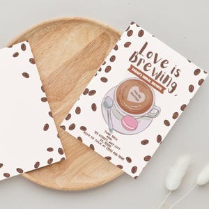 Pode incluir: Convite para chá de panela com tema de café. O convite apresenta o texto "Love is Brewing" e uma xícara de café com um design de coração. Também inclui a data, hora e informações de RSVP.