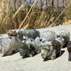 May include: A collection of ten small, intricately carved animal figurines made of green, white, and brown agate. The figurines are all different animals, including a rhino, a bear, and a pig.