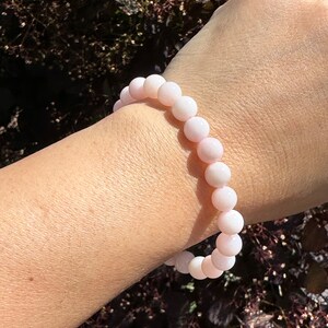 May include: A pink gemstone bracelet with round beads. The bracelet is on a person's wrist.