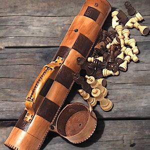 May include: A brown leather chess set case with a checkered pattern and a small leather cup. The case is open and the chess pieces are scattered around it.